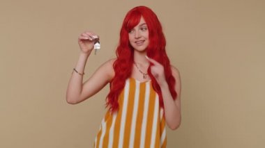 Kızıl saçlı genç emlakçı kadın yeni ev dairesinin anahtarlarını gösteriyor, mülk alıyor ya da kiralıyor, ipotek kredisi veriyor. Kızıl saçlı kızıl kız bej renkli stüdyo arka planında izole edilmiş.
