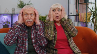 Aman Tanrım. Vay canına. Heyecanlı yaşlı aile büyükbabaları ve büyük anne ve büyük babaları olan erkek kadın kameraya bakarken şaşkınlıkla ellerini kaldırıyor. Ani zaferden şok olmuş bir şekilde. Evde kafası karışmış emeklilerin portresi