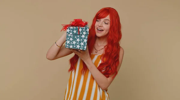 Cheerful redhead young winner woman receive gift box, birthday surprise and expressing great happiness amazement, satisfied with best present bonus. Ginger girl isolated on beige studio background