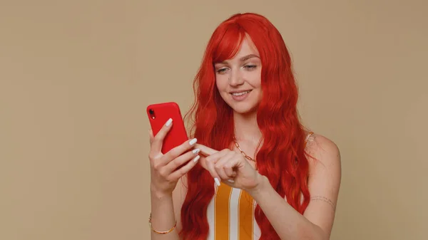 漂亮的红头发女人用手机在网上打印新的帖子短信 搜索成瘾的社交网络 在米色墙壁的背景下 年轻的姜汁女孩被单独拍摄 — 图库照片