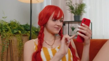 Aman Tanrım. Vay canına. Heyecanlı ve neşeli kazanan kadın akıllı telefon daktilo kullanıyor. Kazanan kazanır. İyi haber zaferi kutlar. Cep telefonlu genç kızıl kız evinde, kanepede oturuyor.