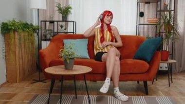 Kablosuz kulaklıklı mutlu, gevşemiş kızıl kız evinde koltukta dans ediyor ve akıllı telefon eğlencesinde en sevilen disko rock n roll müziğini dinliyor. İnsanlar hafta sonu aktiviteleri