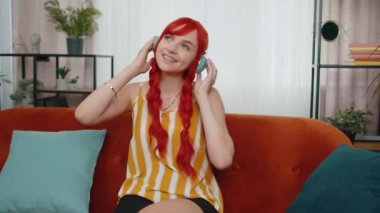 Keyifli, kablosuz kulaklıklı mutlu kızıl kadın evinde koltukta dans ediyor ve akıllı telefon eğlencelerinde en sevilen disko rock n roll müziğini dinliyor. İnsanlar hafta sonu aktiviteleri