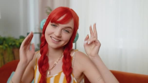 快乐的红头发女人在无线耳机里跳舞 在客厅里唱歌 在移动应用中选择最喜欢的充满活力的迪斯科音乐 在室内娱乐 女孩周末活动 — 图库视频影像