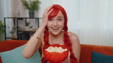 Kanepede oturup patlamış mısır yiyen ve evinde internetten ilginç TV komedi dizileri, filmler, filmler ya da sosyal medya içerikleri izleyen heyecanlı genç bir kadın. Kızıl kız ev eğlencesinden hoşlanıyor.