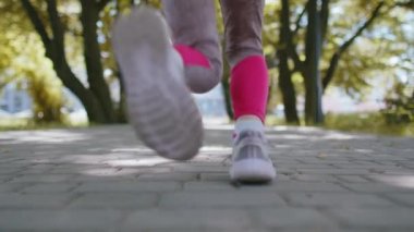 Spora uygun atletik koşucunun, yürümeye yeni başlayan kızın maraton antrenmanının arka görüntüsü. İlerideki yolda kamera önünde koşuyor. Parkta kardiyo çalışması. Çocuk sağlıklı yaşam tarzını seviyor. Etkin çocuklar
