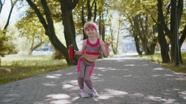 アスレティックスポーツランナーチャイルドガールトレーニングフィットネスエクササイズカメラにブルートゥース音楽スピーカーダンスを聞いて楽しんでいます 公園で心臓を働かせなさい 幼児の子供のジョギングは面白いダンスをお楽しみください アクティブな子供たち — ストック動画