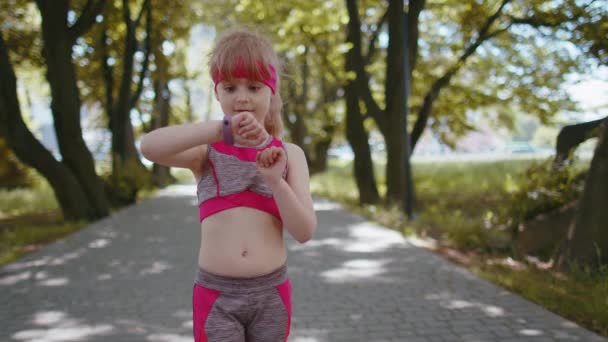 アスレチック幼児ランナーの女の子は ジョギング中のスマートウォッチで時間 心拍数 パルス Spo2をチェックスマートウォッチデバイスフィットネスブレスレットを見てください 朝市公園の外でトレーニングワークアウトカーディオ — ストック動画