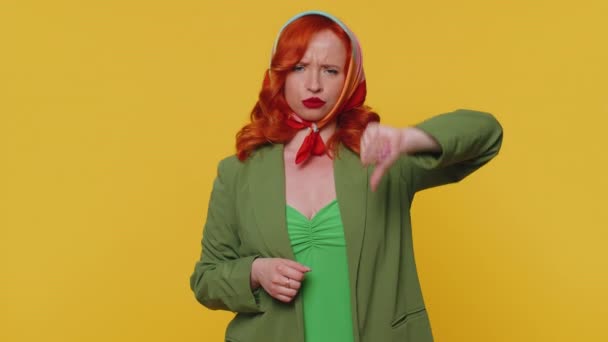 穿着夹克和头巾的不高兴的红头发女人低垂着大拇指的手势 表示不满 不赞成 不满意 不喜欢 年轻的姜汁女孩 黄色背景的室内工作室 — 图库视频影像
