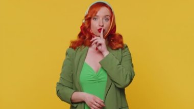 Sessiz olun lütfen. 20 'li yaşlardaki kızıl saçlı kadının portresi işaret parmağını dudaklara bastırıyor. Sessizlik işareti gizli tutulmasını sağlıyor. Sarı stüdyo arka planında yalnız poz veren güzel kızıl kız.