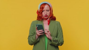 Memnun olmayan kızıl saçlı genç kadın akıllı telefon daktilo kullanıyor. Ani piyango sonuçlarını kaybediyor. Kötü haber, kayıp. Stüdyodaki kızıl kız sarı arka planda izole edilmiş.