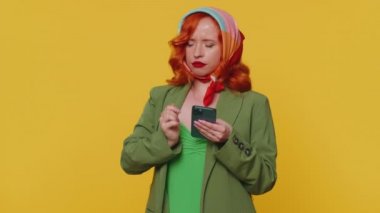 Kaybolmuş, yardıma muhtaç kızıl saçlı genç bir kadın akıllı telefondan doğru adres ya da kafeterya bulmak için online harita kullanıyor. Bir yol arıyor. Yetişkin kızıl kız sarı arka planda kapalı bir stüdyoda izole edilmiş.