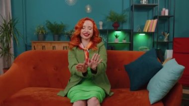 Modayı takip eden, neşeli, pozitif saçlı, dans eden, ritme ayak uyduran, el kaldıran, modern ev dairesinde dublaj yapan genç bir kadın. Kanepede oturan kızıl kız.