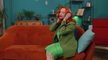 Kablosuz kulaklıklı mutlu, gevşemiş kızıl kız evinde koltukta dans ediyor ve akıllı telefon eğlencesinde en sevilen disko rock n roll müziğini dinliyor. İnsanlar hafta sonu aktiviteleri