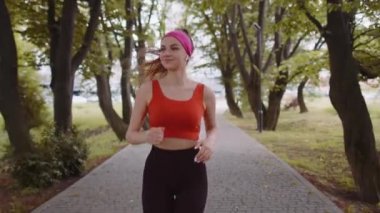 Sportif formda koşucu kız maraton antrenmanı yapıyor, kulaklıkla müzik dinliyor. Sabah parkta kardiyo çalışması var. Sağlıklı yaşam tarzını seven genç bir kadın. Aktif zayıf koşucu sporcu kadın