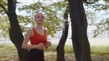 Sporcu spor koşucusu kız maraton koşusu yapıyor, kulaklıkla müzik dinliyor. Sabah parkta kardiyo çalışması var. Sağlıklı yaşam tarzını seven genç bir kadın. Aktif sporcu kadın koşucu