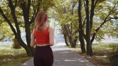 Sporcu spor koşucusu bir kızın maraton antrenmanı, kulaklıkla müzik dinlemesi. Parkta kardiyo çalışması. Genç bir kadın sağlıklı yaşam tarzını seviyor. Aktif sporcu kadın koşucu
