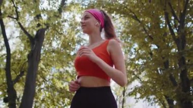 Yavaş hareket eden formda sporcu kız maraton koşuyor, kulaklıkla müzik dinliyor. Sabah parkta kardiyo çalışması var. Sağlıklı yaşam tarzını seven genç bir kadın. Aktif sporcu kadın koşucu