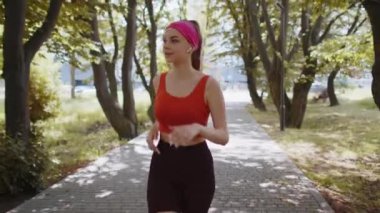 Sporcu spor koşucusu kız maraton koşusu yapıyor, kulaklıkla müzik dinliyor. Sabah parkta kardiyo çalışması var. Sağlıklı yaşam tarzını seven genç bir kadın. Aktif sporcu kadın koşucu