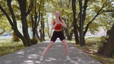 Sıska atletik formda spor kızı çömelme hareketleri yapıyor, kulaklıkla müzik dinliyor. Sabahları parkta spor salonuna giderdik. Sağlıklı yaşam tarzını seven genç bir kadın. Aktif sporcu kadın. Aerobik, kilo kaybı