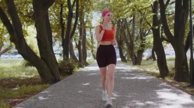Sporcu spor koşucusu kız maraton koşusu yapıyor, kulaklıkla müzik dinliyor. Sabah parkta kardiyo çalışması var. Sağlıklı yaşam tarzını seven genç bir kadın. Aktif sporcu kadın koşucu