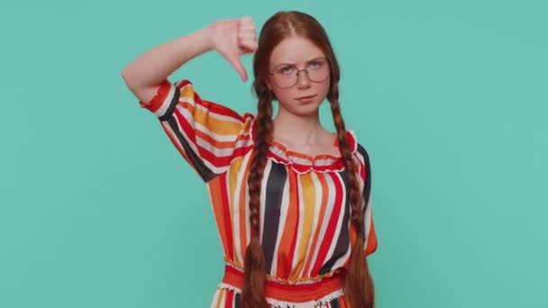 穿着衣服的不高兴的红头发姑娘露出大拇指垂下的手势 表示不满 不赞成 不满意 不喜欢 年轻的生姜少年小孩 蓝色背景的室内演播室 — 图库视频影像