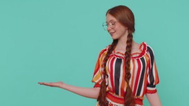 Güzel, kızıl saçlı bir kız, boş bir yeri işaret ediyor, ticari metinler için reklam alanı, ürün tanıtımı için fotokopi alanı. Genç kızıl ergen çocuk. Stüdyo, mavi arka planda kapalı alanda çekildi.
