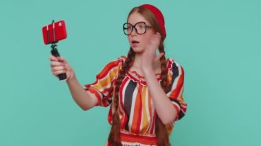 Vay canına. Etkilenmiş kızıl saçlı blog yazarı cep telefonunun selfie çektiği selfie çubuğu abonelerle çevrimiçi video bağlantısı kuruyor. Genç kızıl ergen çocuk mavi stüdyo arka planında izole