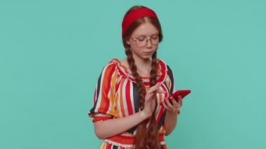 Güzel kızıl saçlı kız cep telefonuyla web mesajlarına yeni mesajlar yazıyor, arama yapıyor, sosyal ağların bağımlılığını araştırıyor. Genç kızıl ergen çocuk stüdyosu mavi arka planda izole edilmiş.