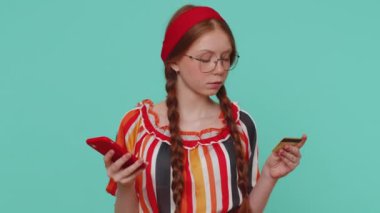 Samimi kızıl saçlı müşteri kredi kartı ve akıllı telefon kullanarak online alışveriş yapıyor, ödeme yapıyor. Finans, internet. Genç bir çocuk mavi arka planda izole edilmiş