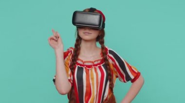 Kızıl saçlı kız, simülasyon gerçekçi oyunu oynamak için kulaklık uygulaması kullanıyor. Sanal gerçeklik 3D 360 video filmi izliyor. VR gözlüklü kızıl saçlı genç çocuk mavi stüdyo arka planında izole edilmiş.