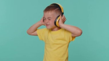 Küçük mutlu çocuk kulaklıkla müzik dinliyor, disko dansı yapıyor, kendini ifade eden eğlenceli elleri var. Genç anaokulu çocuğu mavi stüdyoda tek başına izole edilmiş.