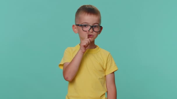 静かにしてください 小さな幼児の子供の男の子は唇に人差し指を押すと 沈黙ジェスチャーのサインは秘密を伝えません 若いです就学前の子供で眼鏡で一人でブルースタジオの背景に — ストック動画
