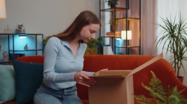 Öfkeli, hoşnutsuz genç kadın paketlerini açıyor üzgün ve kafası karışmış bir şekilde çevrimiçi bir dükkandan gelen yanlış teslimat, evde kötü kalite alışveriş. Kız kapalı bir odada kanepede alışveriş yapıyor.