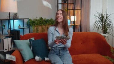 Başarı, galibiyet, gol başarısı, iyi haber, modern ofis binasında piyango talihi kutlayan genç bayana para yağmuru yağıyor. Kariyer büyür. Kız kanepede oturur.