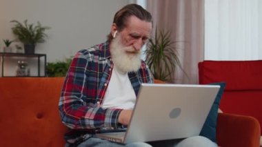 Yaşlı büyükbaba, sınıftaki kanepede dizüstü bilgisayarla çalışıyor. Yaşlı emekli büyükbaba defter üzerinde çalışıyor, mesajlar gönderiyor, online siparişler veya yemek siparişleri veriyor, film seyrediyor.