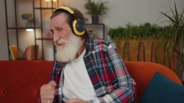 Mutlu, gevşemiş, kablosuz kulaklıklı yaşlı adam evinde koltukta dans ediyor ve akıllı telefon eğlencelerinde favori disko rock n roll müziğini dinliyor. İnsanlar hafta sonu aktiviteleri