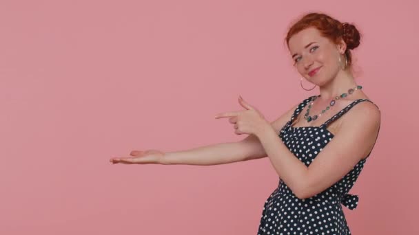 美しい赤毛の女性は 空の場所 商業テキストの広告エリアを指して 商品のプロモーションのためのコピースペースを親指を表示します 若い生姜娘 スタジオはピンクの壁の背景に屋内で撮影 — ストック動画