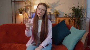 Hey sen! Genç kızıl saçlı kız heyecanlı bir şekilde gülümsüyor ve kamerayı işaret ediyor, şanslı kazananı seçiyor, muhteşem olduğunu gösteriyor, davet ediyor, onaylıyor. Evde oturan çilli çocuk kanepede oturuyor.