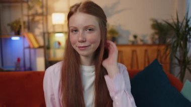 Gülümseyen neşeli, mutlu, kızıl saçlı, göz kırpan, kameraya gülümseyen, göz kırpan ve flört eden, iyimserliğini ifade eden bir kız çocuğu. Evde oturan çilli çocuk kanepede oturuyor.