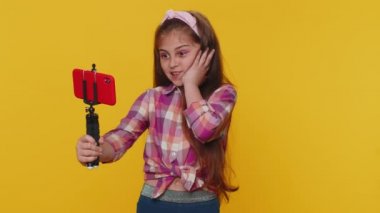 Vay canına. Etkilenmiş genç kız çocuk blogcu cep telefonu özçekim çubuğuyla selfie çekiyor, internetten video bağlantısı kuruyor. Stüdyo sarı arka planda izole edilmiş küçük çocuklar.