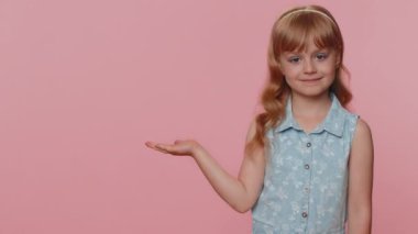 Yürümeye yeni başlayan kız boş yeri işaret ediyor, reklam alanı ticari metinler için, ürün tanıtımı için yer kopyalıyor. Küçük bir çocuk. Stüdyo çekimleri pembe duvar arka planında.