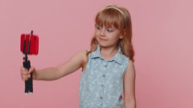 Genç kız çocuk blogcu kız akıllı telefon özçekim çubuğuyla selfie çekiyor abonelerle internet üzerinden video görüşmesi yapıyor. Stüdyo pembe arka planda izole edilmiş küçük çocuklar.
