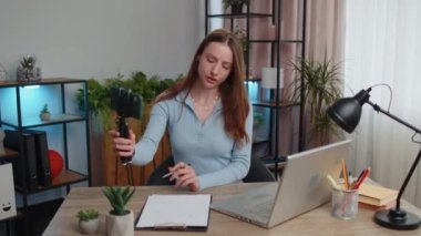 Genç kadın iş kadını blogcu sosyal medya için akıllı telefondan çekim videosu çekiyor. Masada oturmuş gülümsüyor ve ev ofisinden çalışıyor. Kız serbest çalışma, e-öğrenme, internetten uzak iş