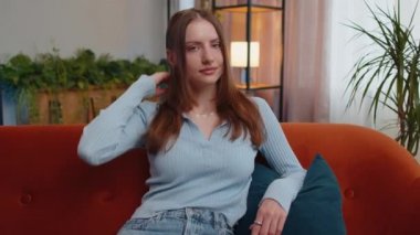 Close-up portrait of happy smiling young woman in blue blouse, looking at camera. Pretty beautiful brunette girl indoors isolated at home in living room sitting on couch alone. Female nature beauty