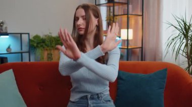 Stop gesture. Angry woman say No hold palm folded crossed hands, warning of finish, prohibited access, declining communication, body language, danger. Girl in home living room sitting on sofa indoors