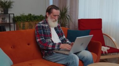 Yaşlı büyükbaba, sınıftaki kanepede dizüstü bilgisayarla çalışıyor. Yaşlı emekli büyükbaba defter üzerinde çalışıyor, mesajlar gönderiyor, online siparişler veya yemek siparişleri veriyor, film seyrediyor.