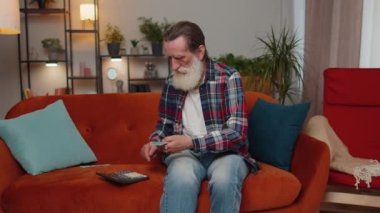 Planlama bütçesi. Zengin, mutlu büyükbaba para sayıyor, hesap makinesi kullanıyor ve evdeki faturaları hesaplıyor. Gelir getiren, kazanan, planlı tatil için para biriktiren, hediyeler alan bir adam.