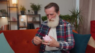 Zavallı yaşlı büyükbaba, elinde kumbarası ve bir dolarlık banknotla, yetersiz miktarda para tutuyor. Finansal kriz. İflas. Yoksulluk ve yoksulluk. Oturma odasındaki kanepede oturan yaşlı adam.