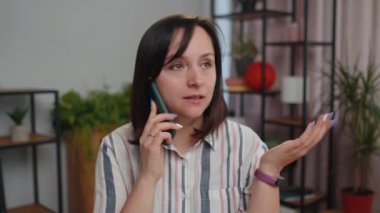 Young woman freelancer sits at desk at home office answering to client on mobile phone call, using smartphone. Conversation. Adult pretty girl student study working online remote distance job, talking